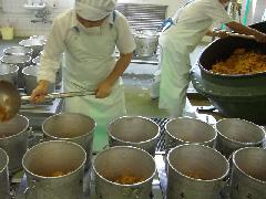 白色の作業着を着たスタッフ2名が、チキンライスを食缶に分けている写真
