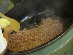 大きな釜に投入した鶏肉に塩こしょうをしながら大きな木べらで炒めている写真