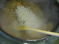 大きな釜に入れた鶏肉に他の具材を投入し、さらに炒めている写真