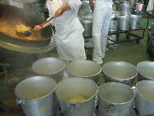 クラス別の食缶を並べて出来上がった五目ごはんを次々取り分けている写真