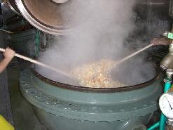 大きな釜に肉以外の他の材料も入れてさらに炒め左右からかき混ぜている写真