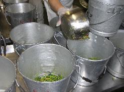 バケツのような食缶を並べて鍋を使って入れている写真