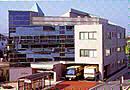 手前の3階建ての建物内に2台のバスが入れられるような造りになっていて、その手前にはバス停も設置されている、奥にガラス張りの窓が前方に見える大きな建物の長久手市保健センターの写真