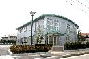 手前に大きな街灯があり、薄緑色の丸みを帯びた屋根の二階建てのまちづくりセンター建物外観の写真