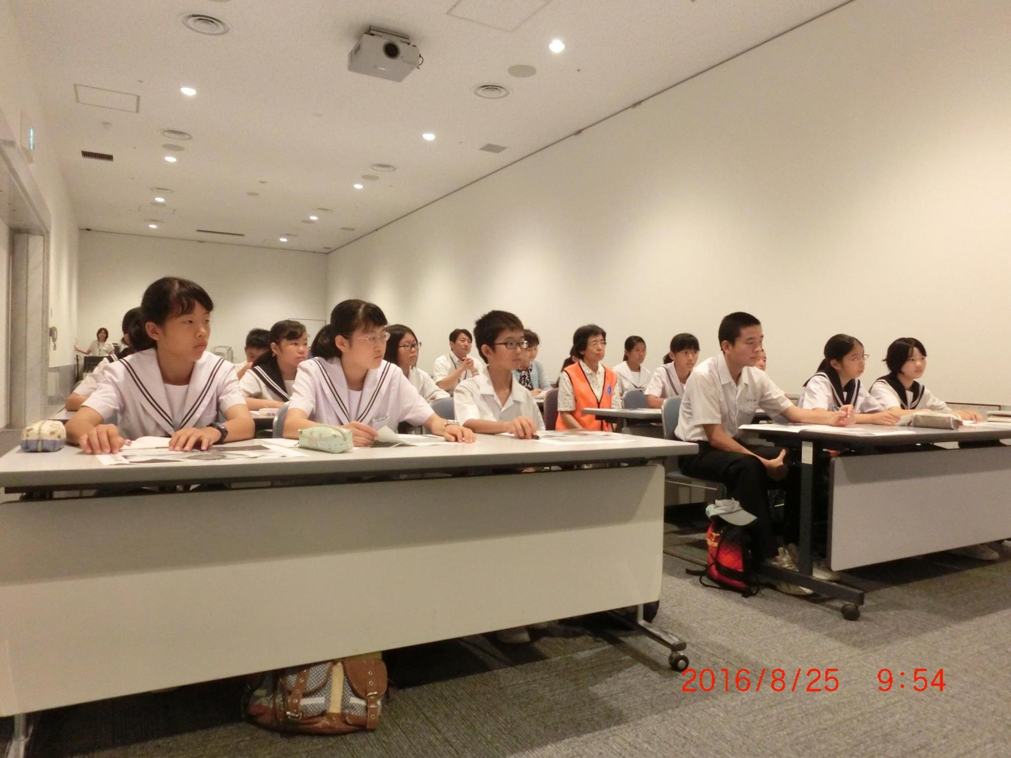 生徒達が長机の席について、熱心に話を聞いている様子の写真