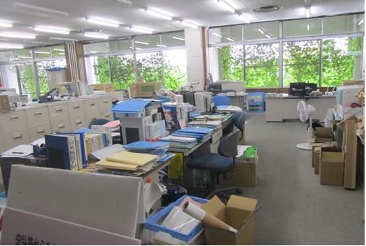 デスクに沢山のファイルがあり、デスクの足元には段ボールが置いてある経営企画課事務室の写真