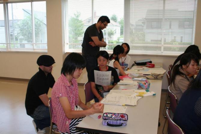 机の上に置かれた資料を見ながらフランス語研修を受けている生徒たちとその様子を傍で見ている留学生の写真