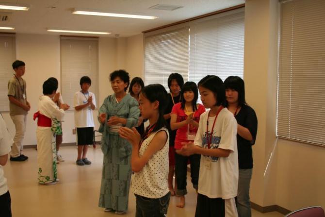 縦に並んで手をたたき長久手音頭を踊っている生徒たちと傍で見ながら教えている2人の女性講師の写真