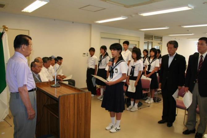 演壇に立っている町長と、町長と向かい合って立ち誓いのことばを述べている団員の女子生徒の写真