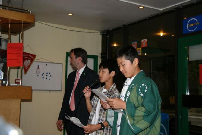 スーツ姿の男性の横に立ち、フランス語でスピーチをしている2人の男子生徒の写真