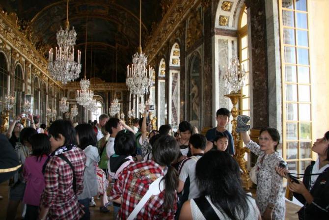 大きなシャンデリアや窓のあるベルサイユ宮殿の内部を見学している生徒たちの写真
