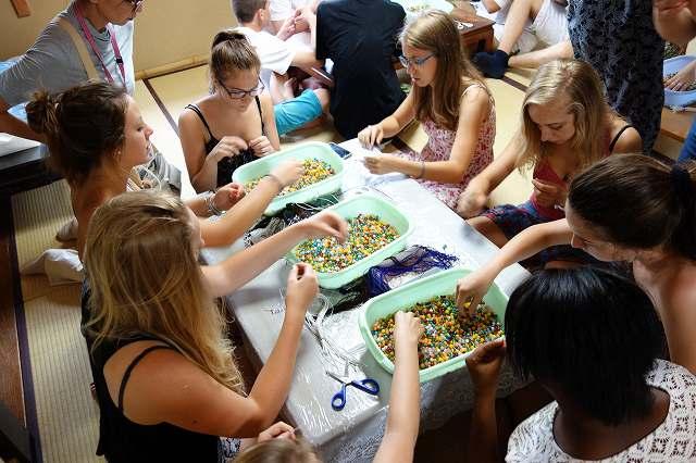 紐にいろいろな色の石を通して数珠を作っているワーテルロー市訪問団の学生たちの写真