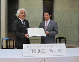 磯見輝夫学長と加藤梅雄町長が協定書を広げて持って並んで写っている写真