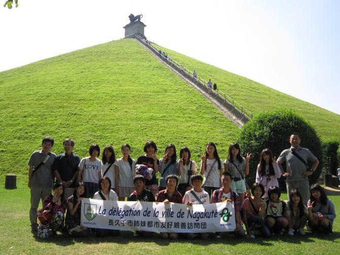 階段が上へと伸びている緑の丘の前で記念撮影をしている青少年派遣団の写真