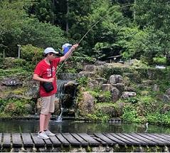 赤いティーシャツを着た男の子が釣り竿を垂らして魚釣りをしている写真