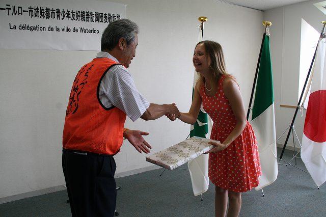 ワーテルロー市訪問団の代表の女性が左手に記念品を持ち、右手で市長と握手を交わしている写真