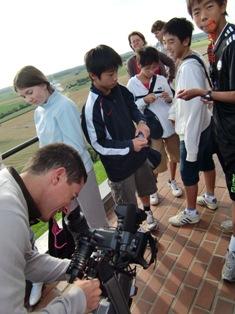 大きなカメラをもって生徒たちを撮影している男性の写真
