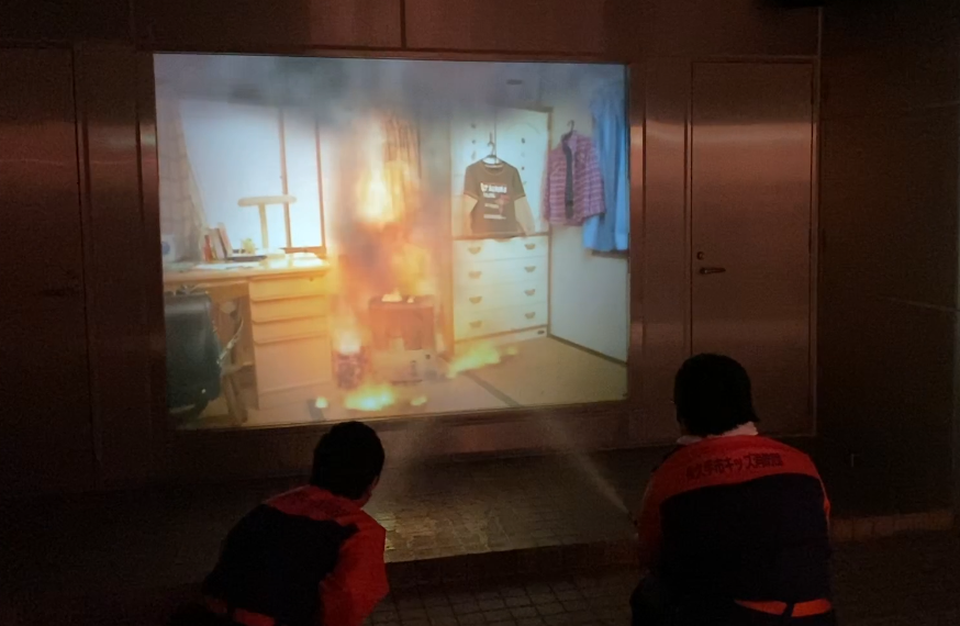 長久手市キッズ消防団の子供たちがスクリーンに映っている火事の火に向かって消火している写真