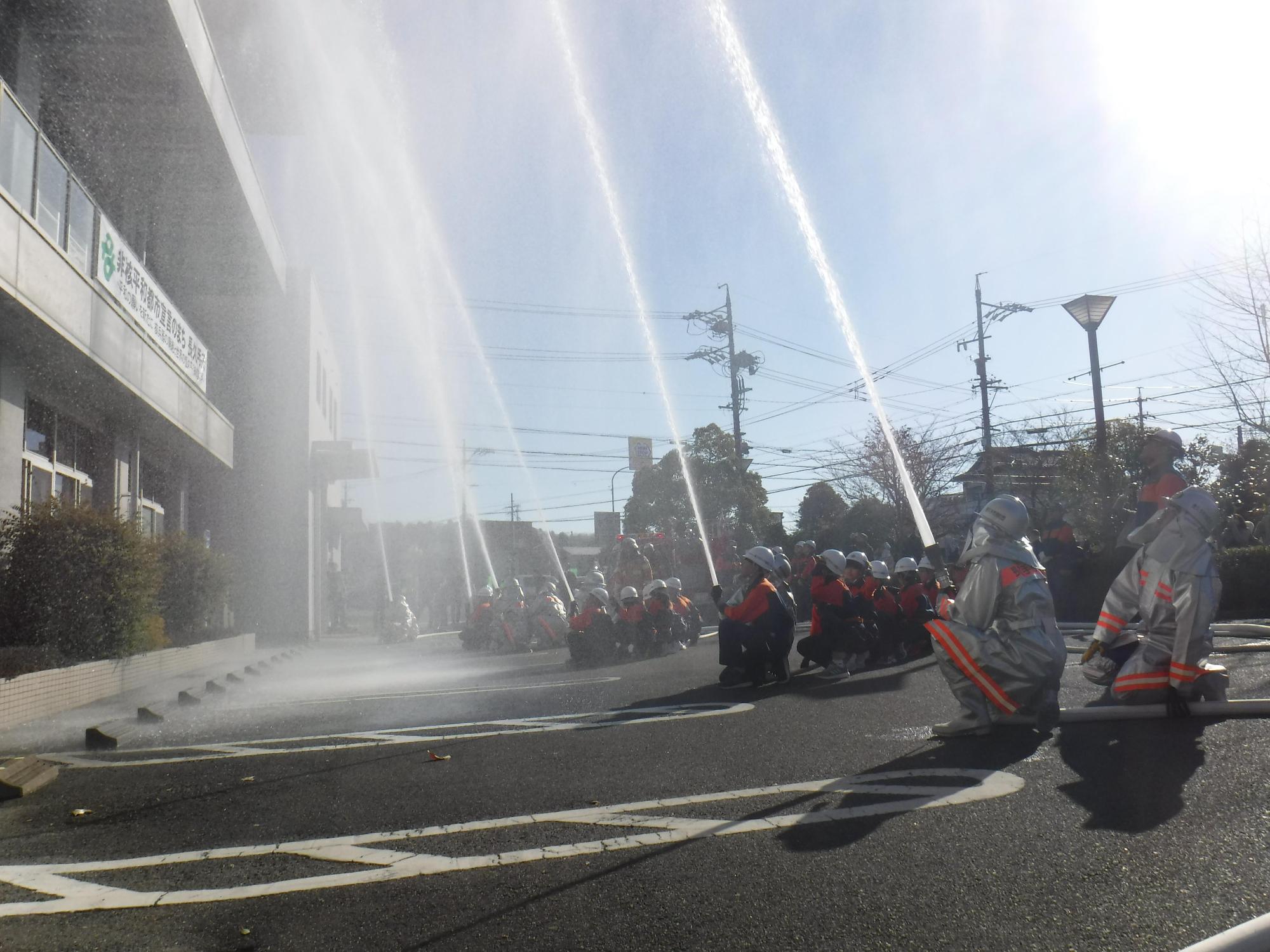 消防団員たちが建物に向かって放水している様子を横から撮影している写真