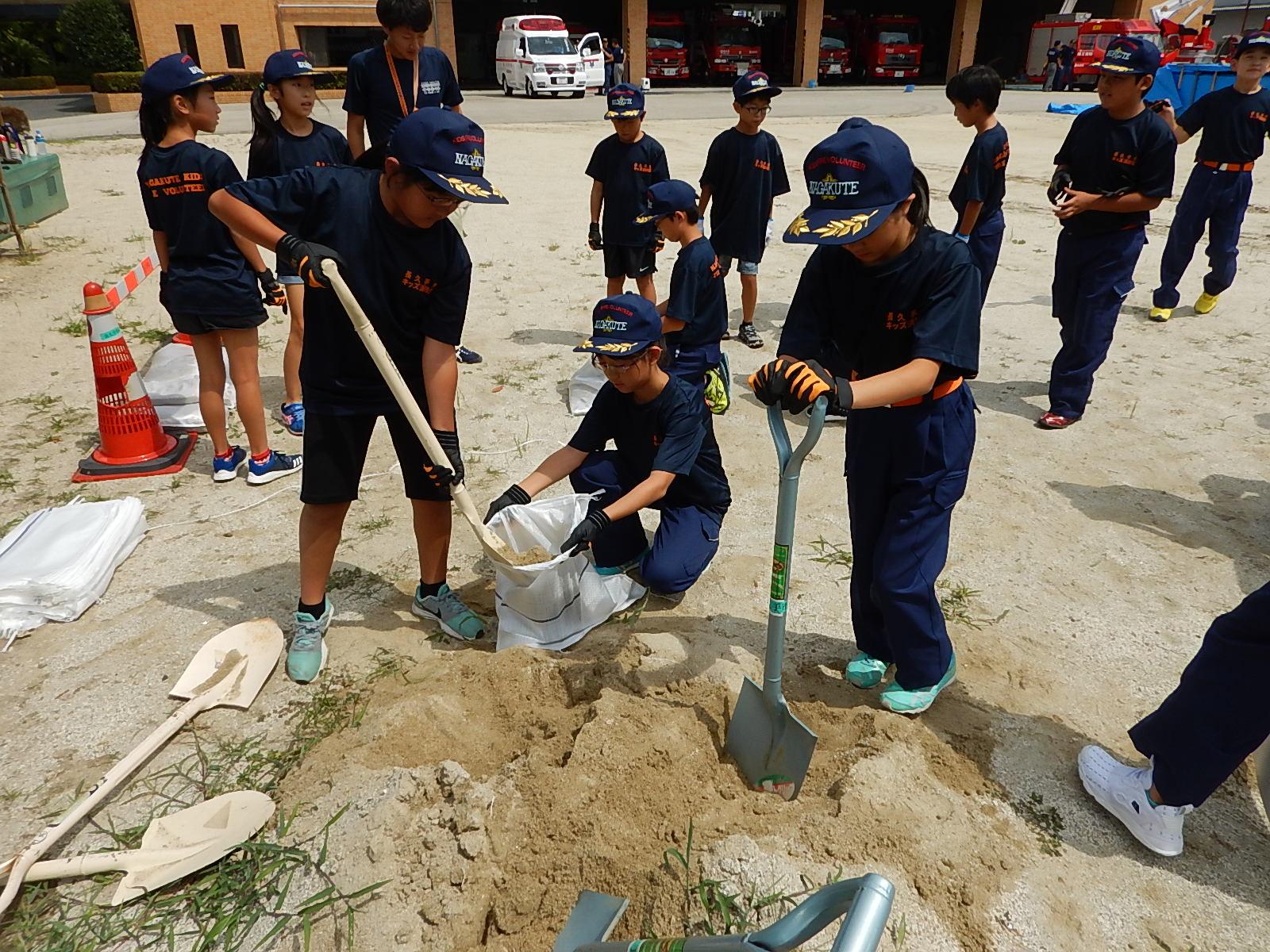 キッズ消防団員たちがスコップで土のう袋に砂を入れている写真