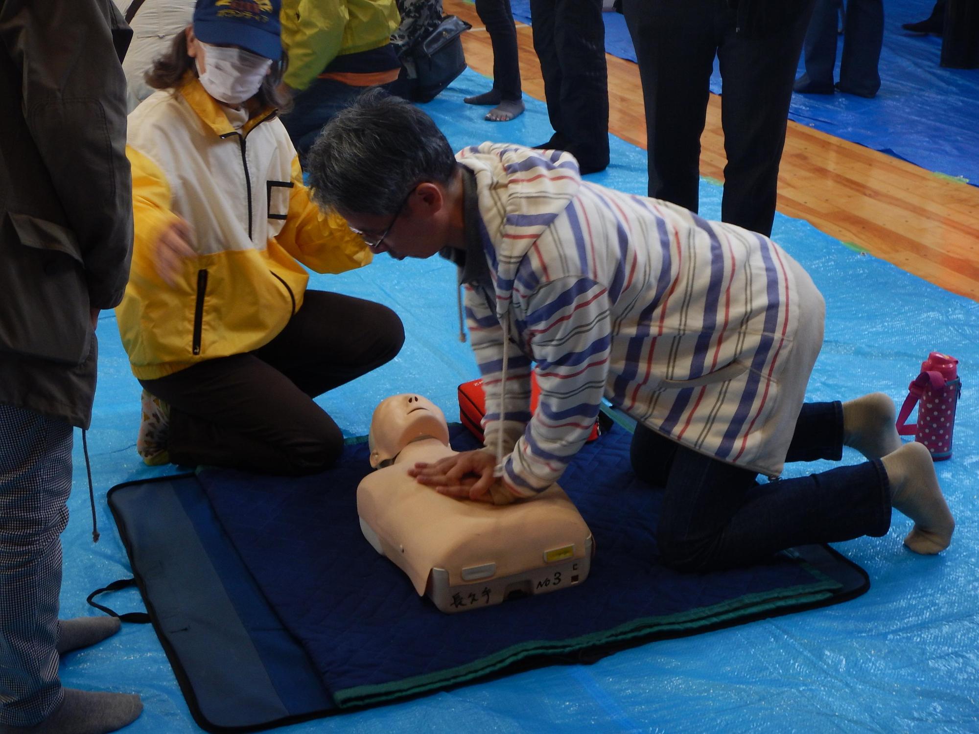 応急救護ボランティアスタッフ指導の下、人形で心肺蘇生訓練を行う参加者の写真