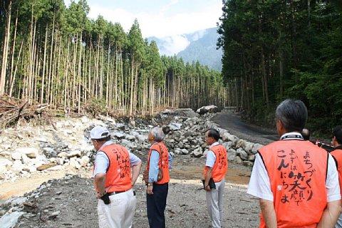 堤防が壊れ泥水が流れて、木々が倒れている災害現場を視察する長久手市自治会連合会長と区長会の代表者4名の写真