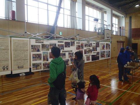 体育館の中の壁に展示された、消防団活動のパネルを見ている参加者の親子の写真