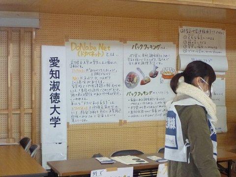 体育館の中の壁に、愛知淑徳大学の学生が作成した大きな模造紙に絵付きで描かれているパッククッキングについての紹介が展示されている写真