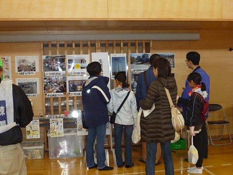 体育館の壁に掲載されているパネルや防災用品の展示を参加者が見ている写真