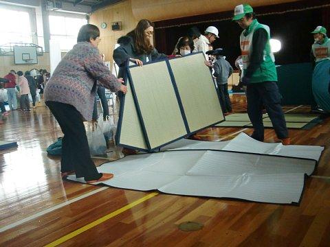 （西小）体育館にて防災資機材の設営訓練で参加者が折り畳を床に敷いている写真