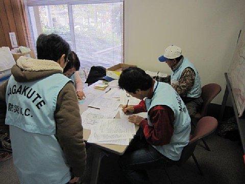 （福祉の家）水色のベストを着たボランティアスタッフたちが机に資料を広げて作業している写真