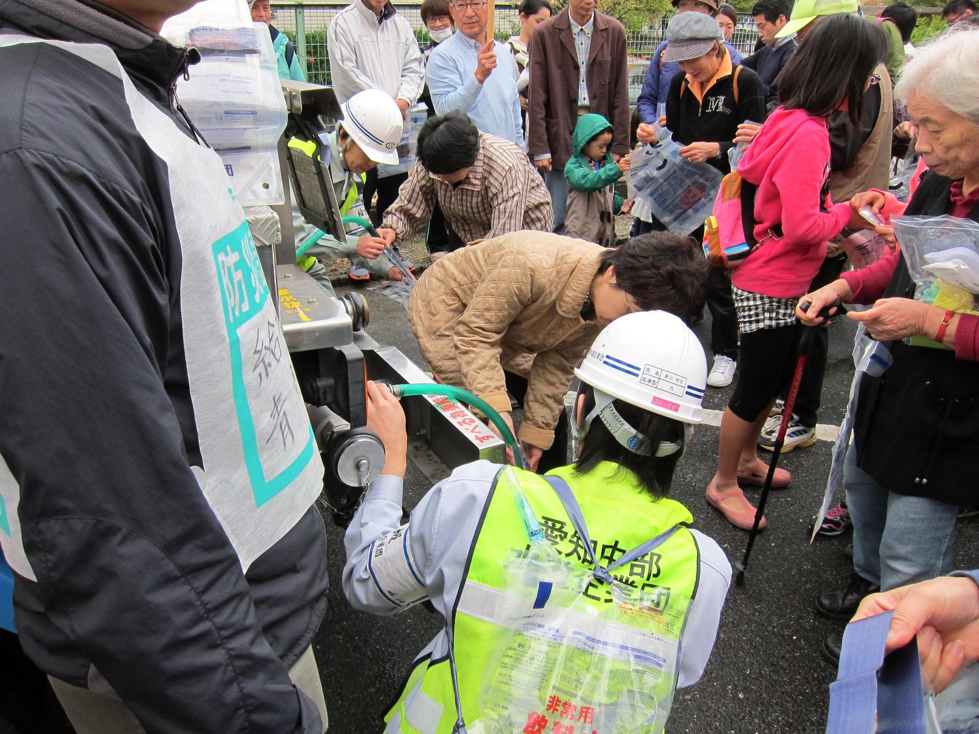 ヘルメットを被った愛知中部水道企業団スタッフと参加者たちが給水袋にタンクの水を給水している写真