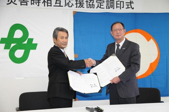 長野県木曽郡南木曽町の町長と市長が左手には協定書を広げて見せ、右手でしっかりと握手をしている写真
