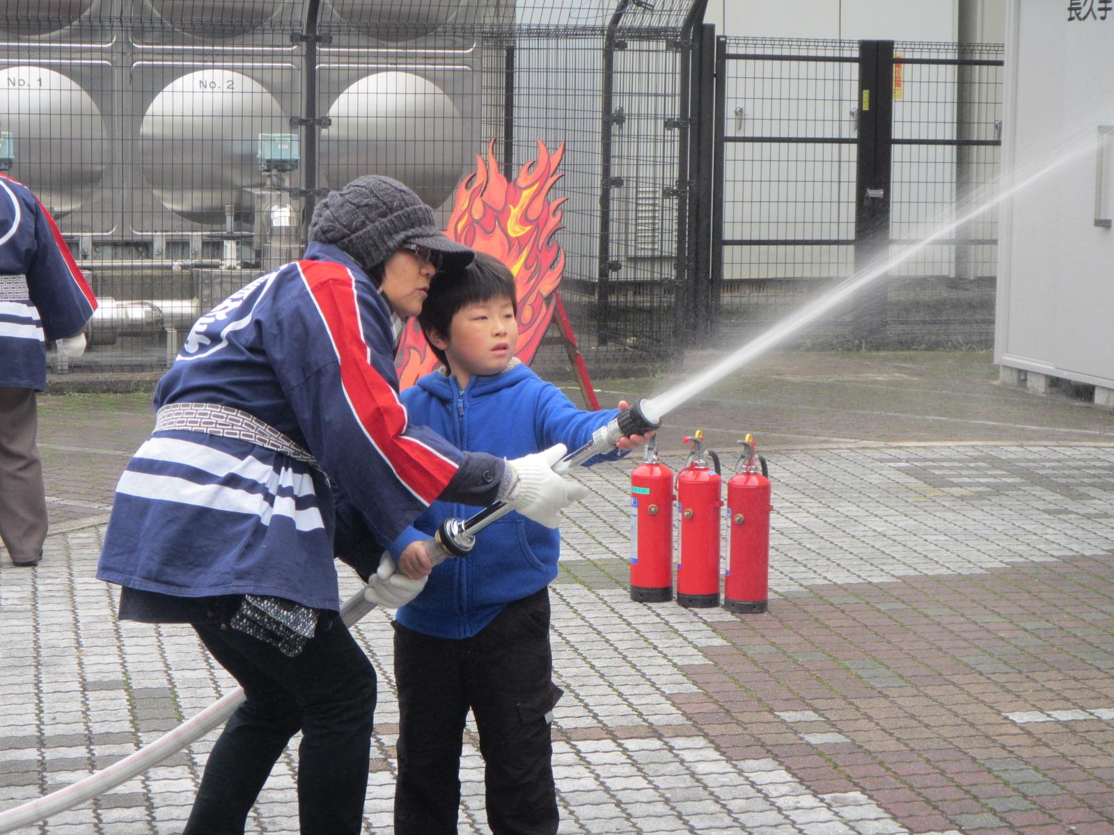 長久手市女性消防クラブ員と一緒にホースを持って放水作業をする子供の写真