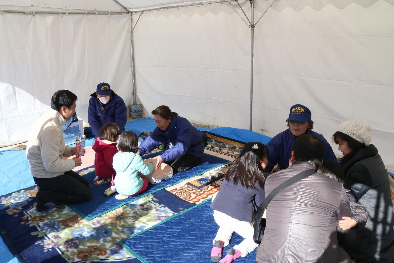 テントの中に毛布などが敷かれた応急救護ボランティアブースで参加者がスタッフに話を聞いている写真