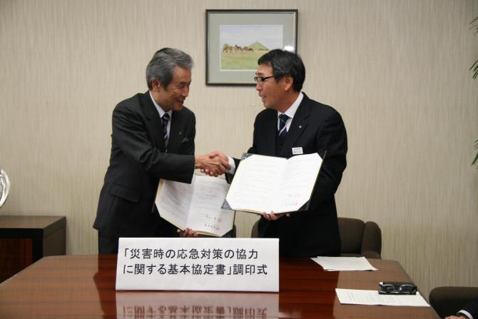 左手で協定書を持ち、右手で握手をしている市長と男性1名の写真