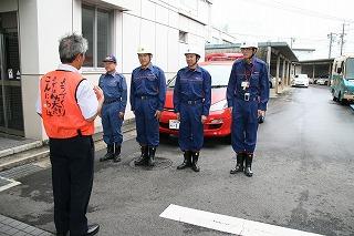 支援隊4名がオレンジ色のベストを着た役員に消防車両の前で出発の挨拶をしている写真