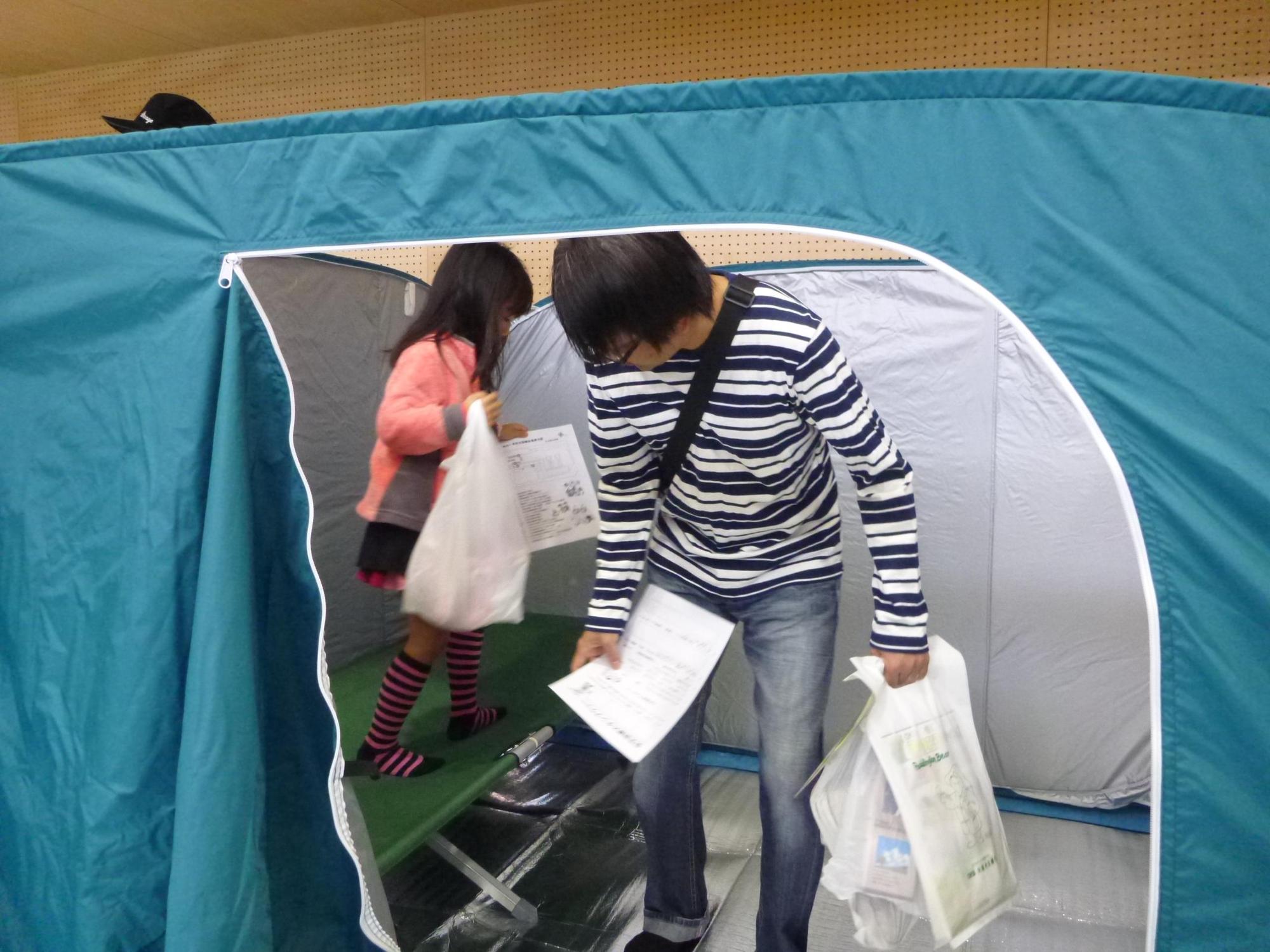 間仕切りされた避難所のテントの中を見て回る親子の写真