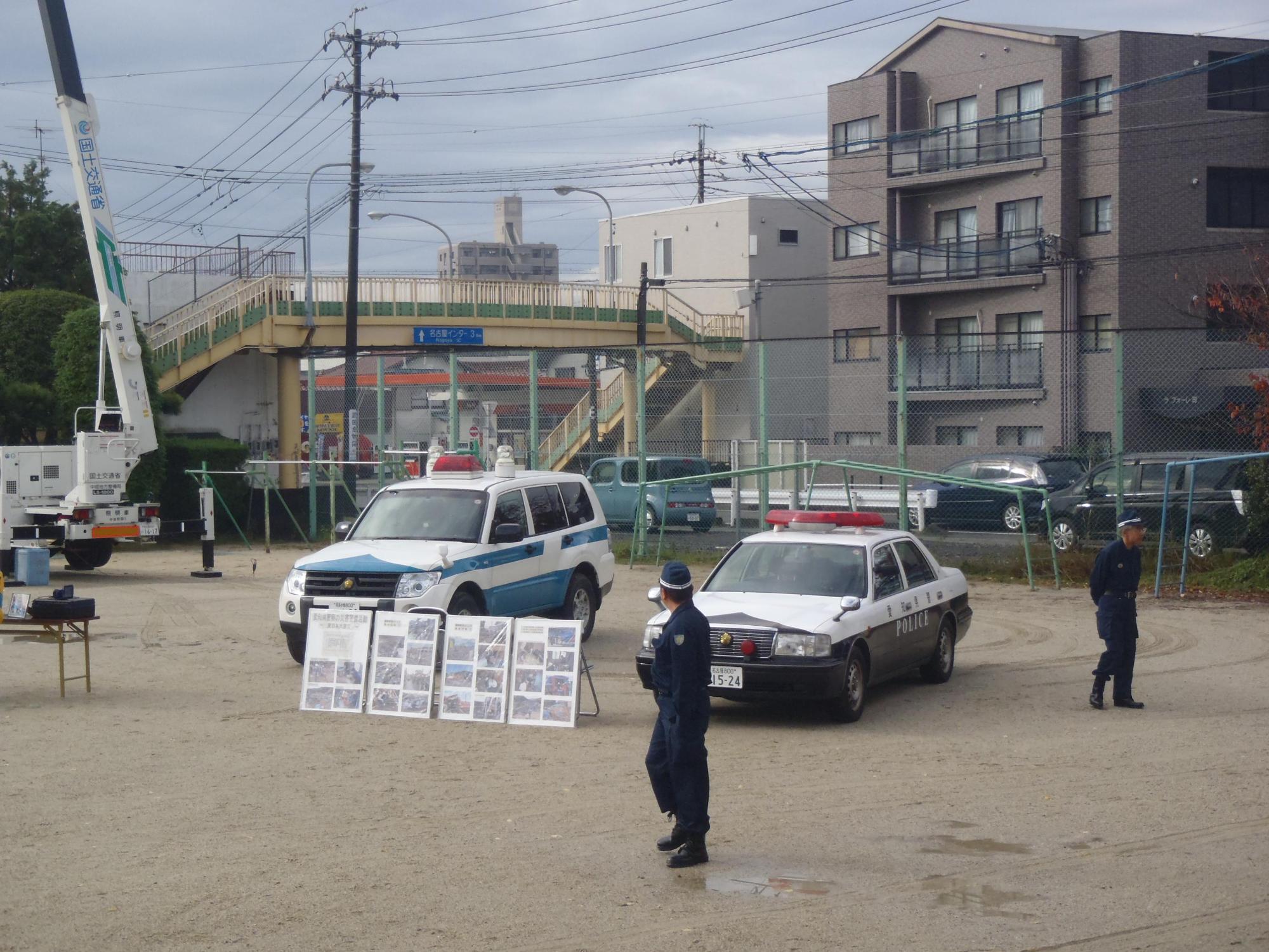 校庭に展示された警察車両の前にパネルが展示されている周りにスタッフが立っている写真