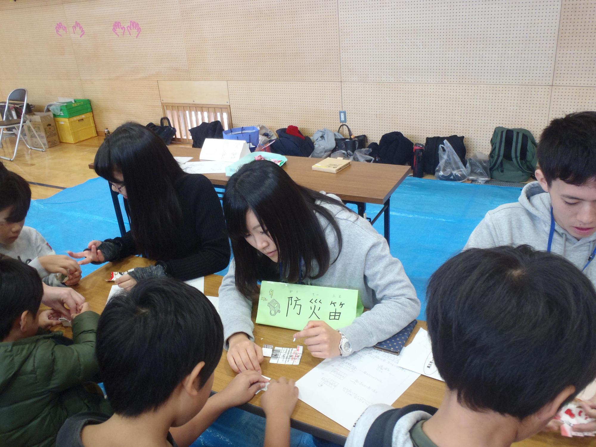 愛知淑徳大学の大学生に教わりながら子供たちが紙で防災笛を作っている写真
