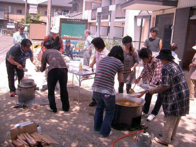 屋外に設置された鍋でご飯を炊いたりカレーを作っている訓練参加者たちの写真