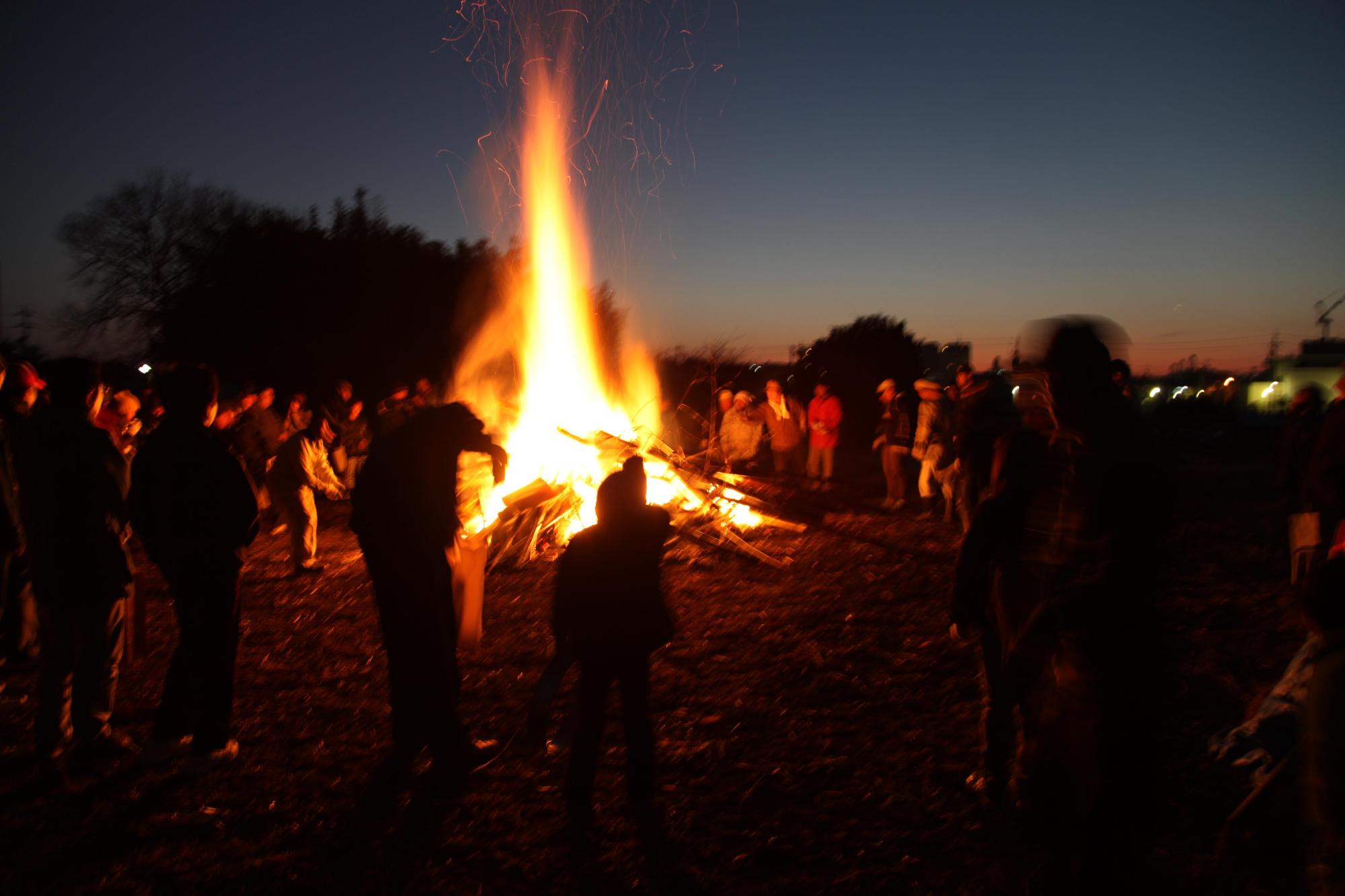 大きく燃え上がっている火の周りに人が集まっている写真