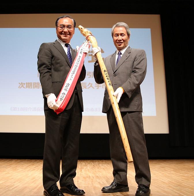 白い手袋をはめた岩沼市長と長久手市長が長久手市長の背丈と同じくらいの長さの「転ばぬ先の杖」を持って写っているいる写真