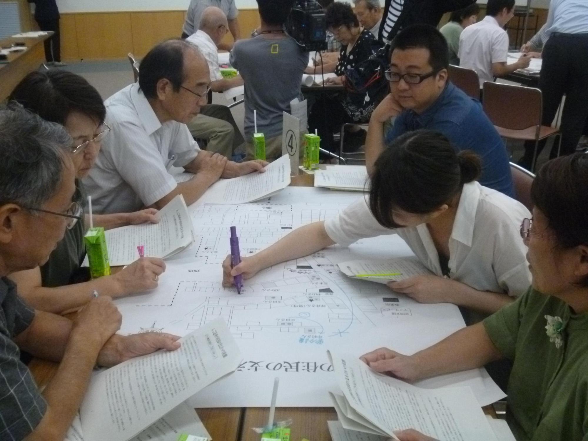 グループで話し合いが行われており、中央の女性が地図にマジックで文字を書き込んでいる写真。