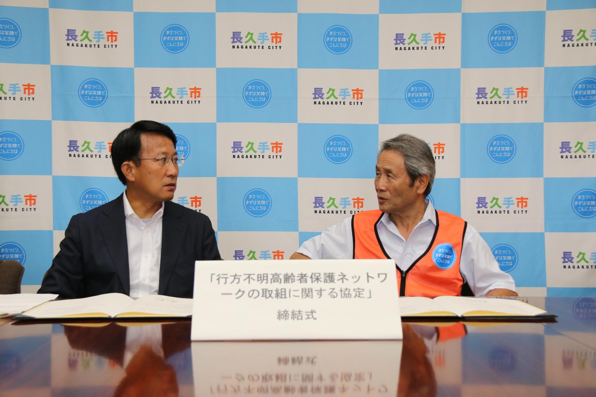 調印式にてひまわりネットワークの小野社長と市長が並んで座っておりお互いの顔を見て話をしている写真