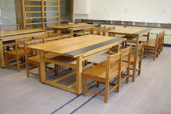 木の机が4台とそれぞれの机に6脚の木の椅子が置かれており、奥には手洗い場が設けられている工房の写真