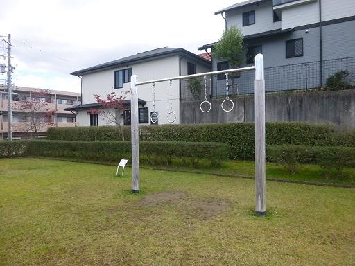 芝生が植えられており、大きな鉄棒のような遊具が設置され、後方に住宅が写っている写真