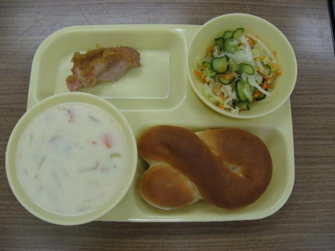 給食トレーの上に、チキンのりんごソースかけ、クリームスープ、フレンチサラダ、クロスロールパンが乗せてある写真