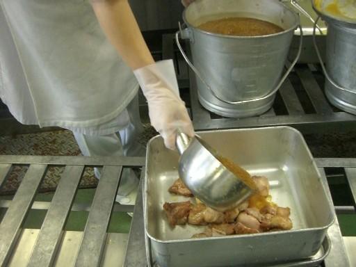 バットに入れた鶏肉に小型鍋を使ってソースをかけている写真