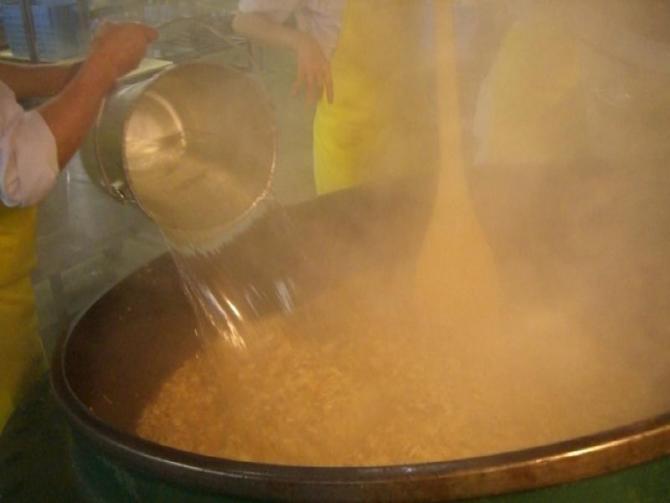 白い作業着に黄色のエプロンを着用したスタッフが、炒めた材料が入っている大きな釜の中に、食缶に入れた水を大量に投下している写真